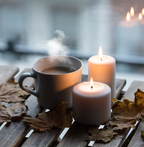 candles and a cup of code in the window with fall leaves