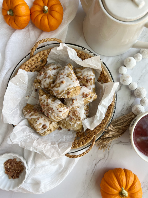 pumpkin scones in a shallow basket with a white teapot and orange pumpkins
