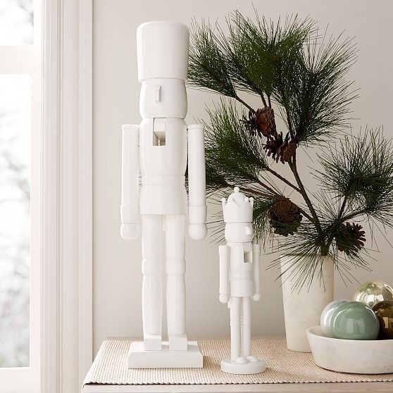 white lacquer nutcracker two on a table with a branch of greens with pinecones