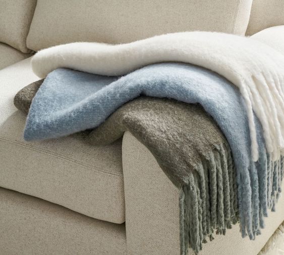 ivory, light blue and gray throw blankets on a ivory sofa. 