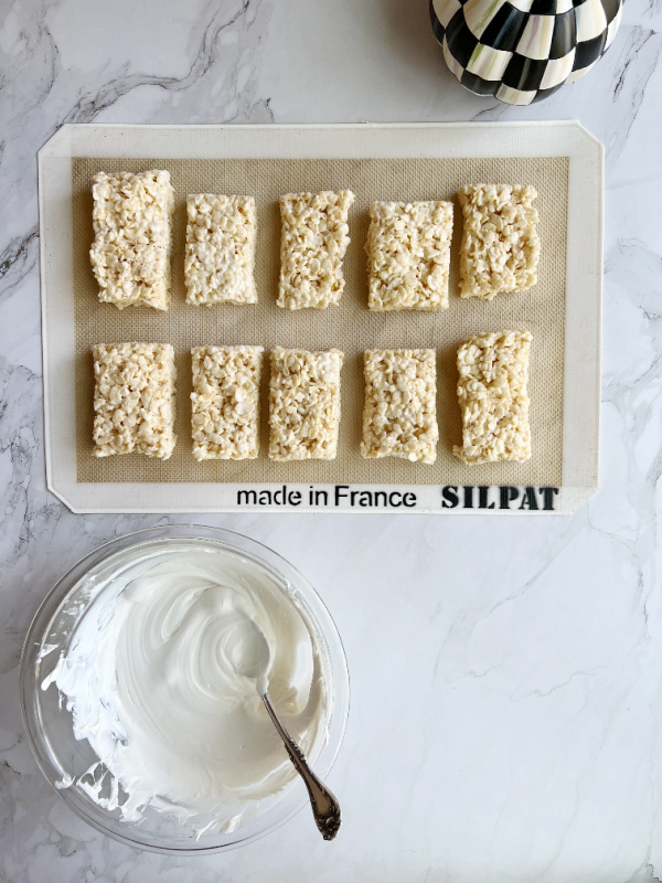Rice Krispie treats on a baking mat with a bowl of white chocolate