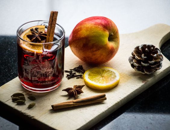 Mulled wine in a cutting board with spices, a lemon slice, an apple and pine cones. 