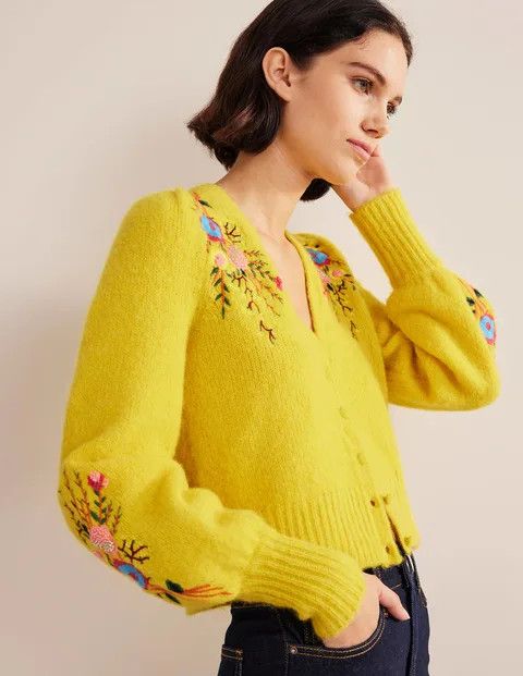 A woman wearing a bright yellow sweater with colorful embroidery. 