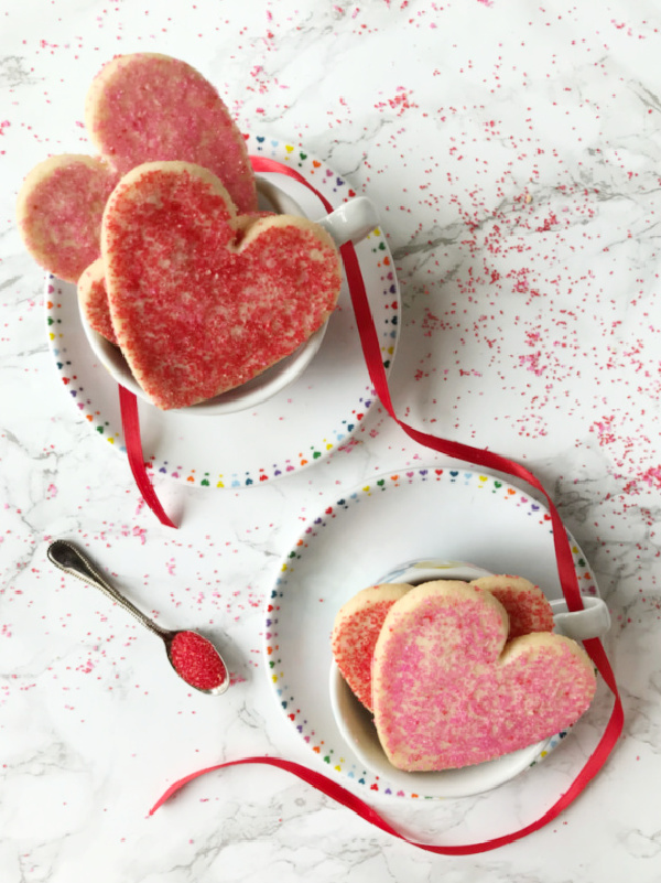 Valentine's Day sugar cookies with red and pink sugar in white tea cups with hearts around the rim. 