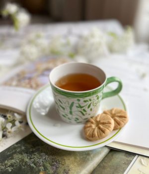 Green and white cup on a saucer filled with tea siting on pile of books.