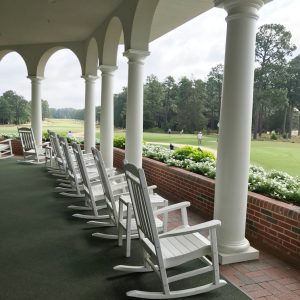 A row of white rocking chairs on a porch overlooking a golf green.