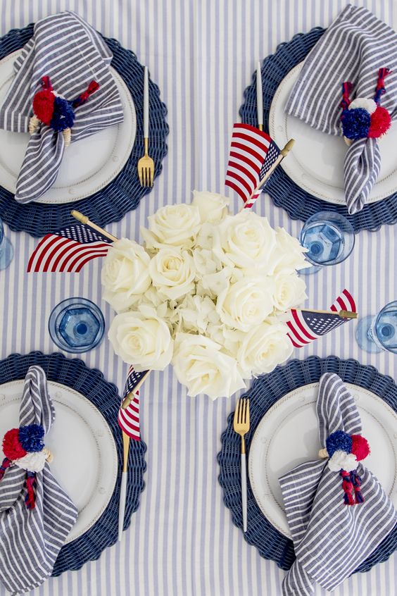 Red white and blue tablescape with white plates, blue chargers, white carnations and little American flags.