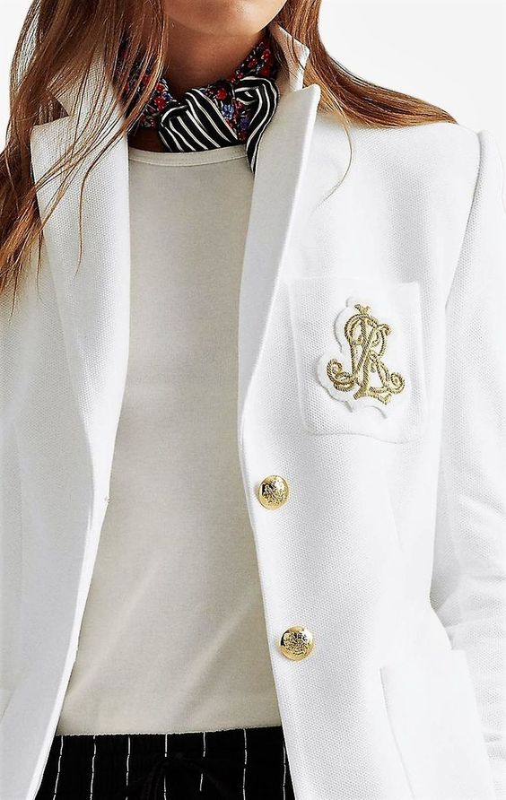 Woman wearing a white shirt, blazer with a blue and white scarf. 