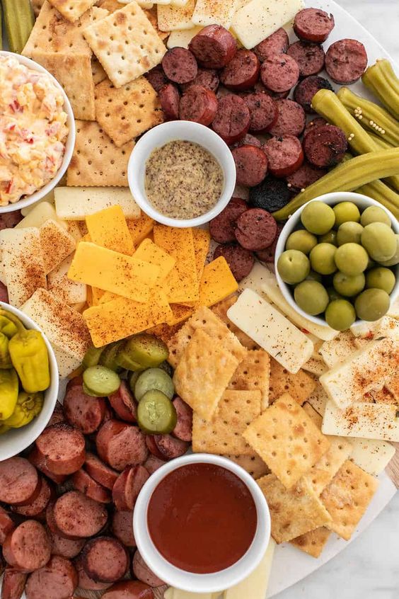 meat and cheese board with bowls of olives, okra, cheese and crackers. 