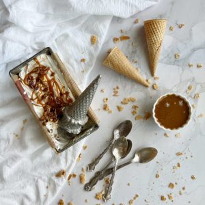 Salted Caramel Candied Pecan "No Churn" Ice Cream in a loaf pan with a bowl of caramel and cones laying by the side.