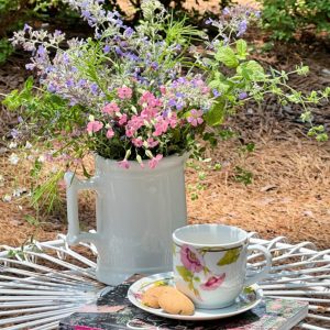 wildflowers in a white pitcher with a cup of tea and a cottage garden book