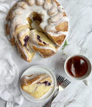 Bonne Maman Blueberry Swirl Bundt Cake on a platter and a plate with a cup of tea.