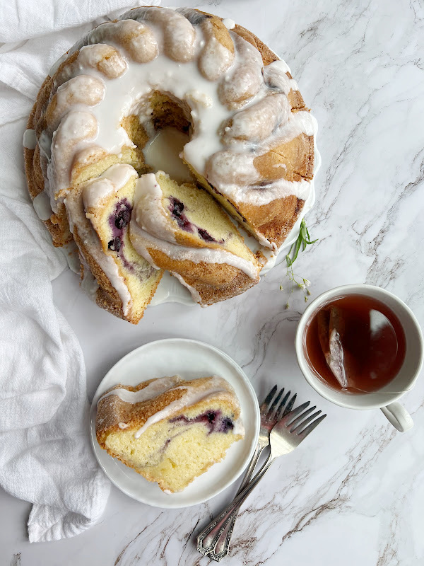 Bonne Maman Blueberry Swirl Bundt Cake on a platter and a plate with a cup of tea.