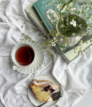 cup of tea with a piece of coffee cake and a pile of books.
