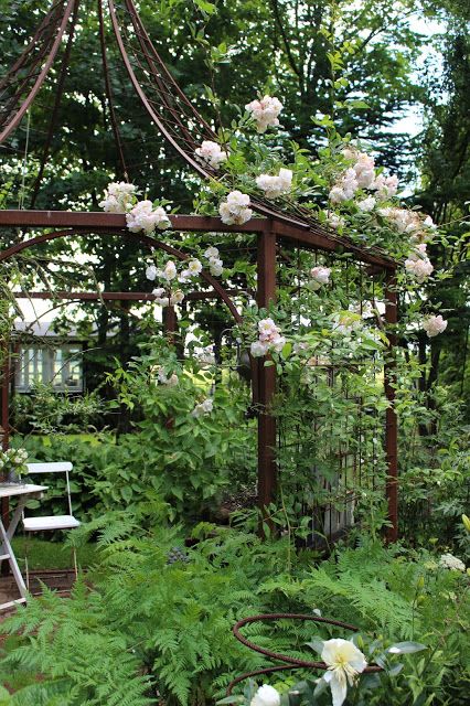 A beaitufil green and white "room" in an English garden with a metal trellis. 