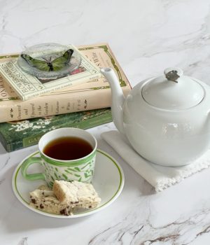 A green and white cup on a white saucer with a white teapot and a pile of gardening books.