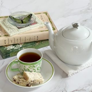 A green and white cup on a white saucer with a white teapot and a pile of gardening books.