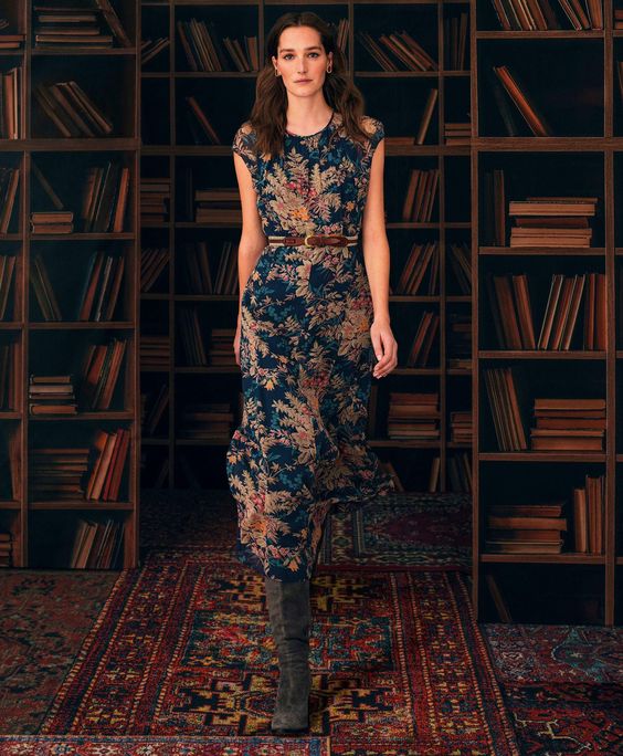 Woman walking in a library wearing a tapestry print dress. 