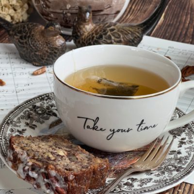A cup that says take your time filled with tea and a piece of chai spiced bread.