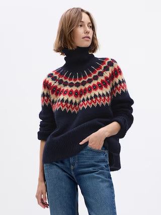 A woman wearing jeans and a blue, pink, red fair isle sweater. 