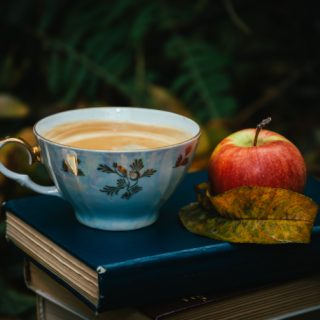 a teacup on top of a book next to an apple.