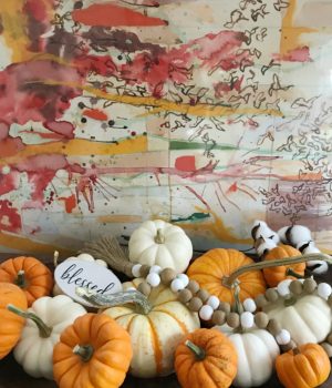 white and orange pumpkins in a wood bowl with an abstract piece of art