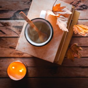 cup of tea on stack of books with fall leaves and a candle.