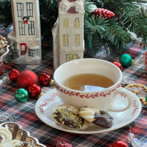 cup of tea and viennese whirl cookies with christmas decorations including 2 victorian houses and ornaments.