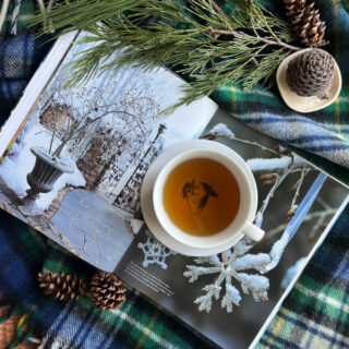 winter flatlay with a tartan blanket cup of tea and an open book