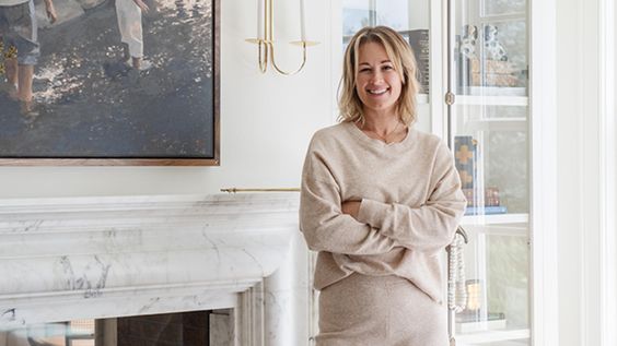 Woman in tan outfit in front of a fireplace. 