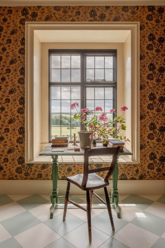 desk in front of a window with a geranium in a pot. 