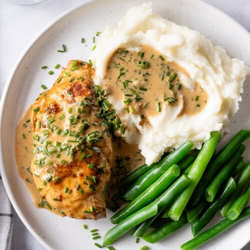 Creamy chive chicken, mashed potatoes and green beans on a white plate. 