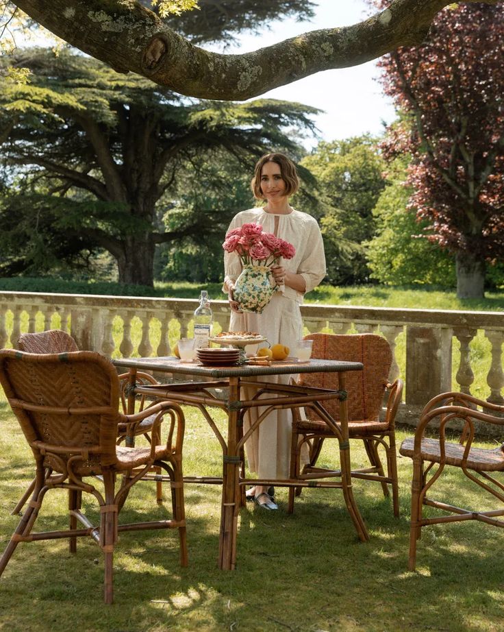 Woman wearing a romantic ivory colored dress standing next to an outdoor table holding flowers. 