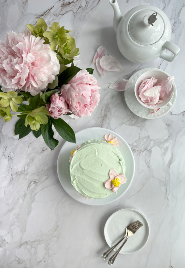 Hersheys chocolate cake with buttercream frosting and a white pot of tea with a cup filled with peony petals and a vase of pink peony flowers