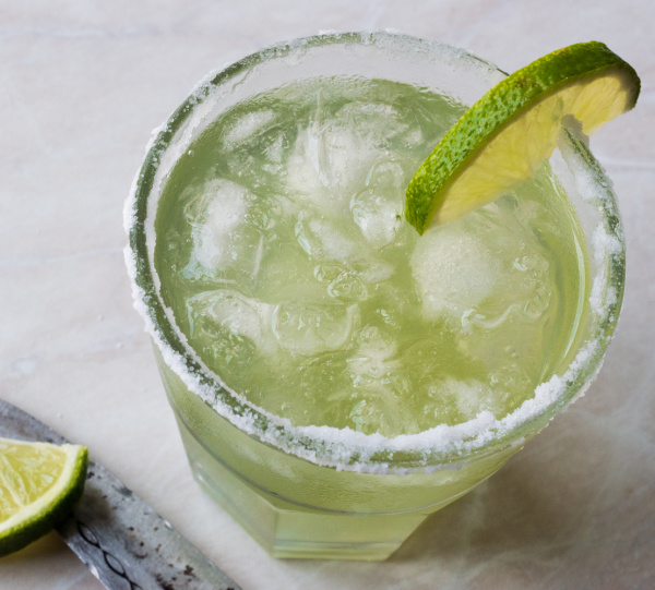 fresh lime margarita in a glass with ice and a knife and lime slice on the left side and a lime slice on the rim. 