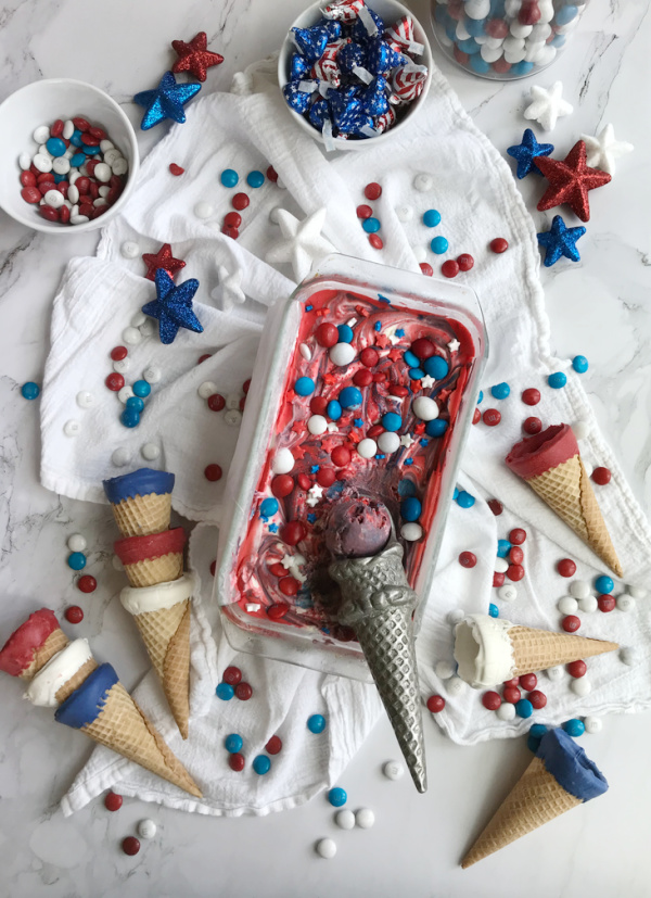 Flatlay of no-churn red white blue ice cream with patriotic candy scattered around including m&M's and Hersheys Kisses.