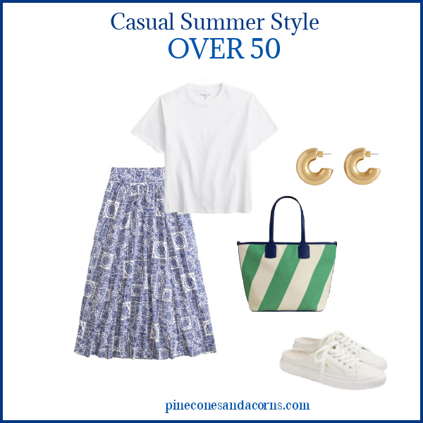 Over 50 Fashion Summer Skirt Outfit with blue and white skirt, white t-shirt, white mule sneakers, gold earrings and a green and white stripe bag. 