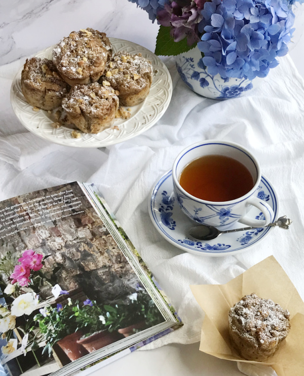banana nut muffins with streusel with a cup of tea in a blue and white cup and a colorful garden book