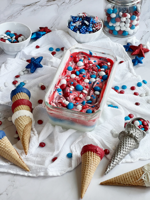 red white blue ice cream in a loaf pan with sugar cones and bowls of patriotic m&m's and candy. 
