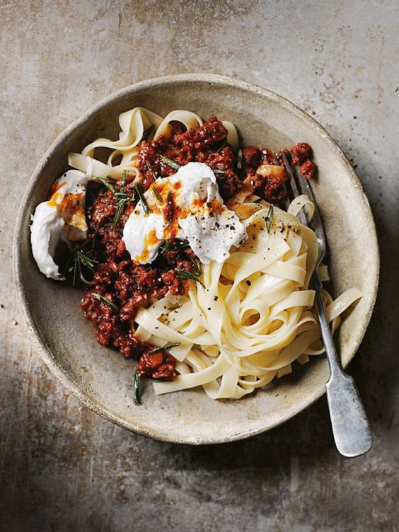 CHORIZO BOLOGNESE with buffalo mozzarella in a tan pottery bowl with a fork. 