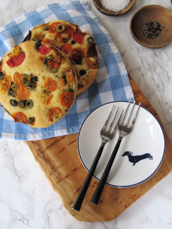 A wood board with tomato focaccia bread and a plate. 