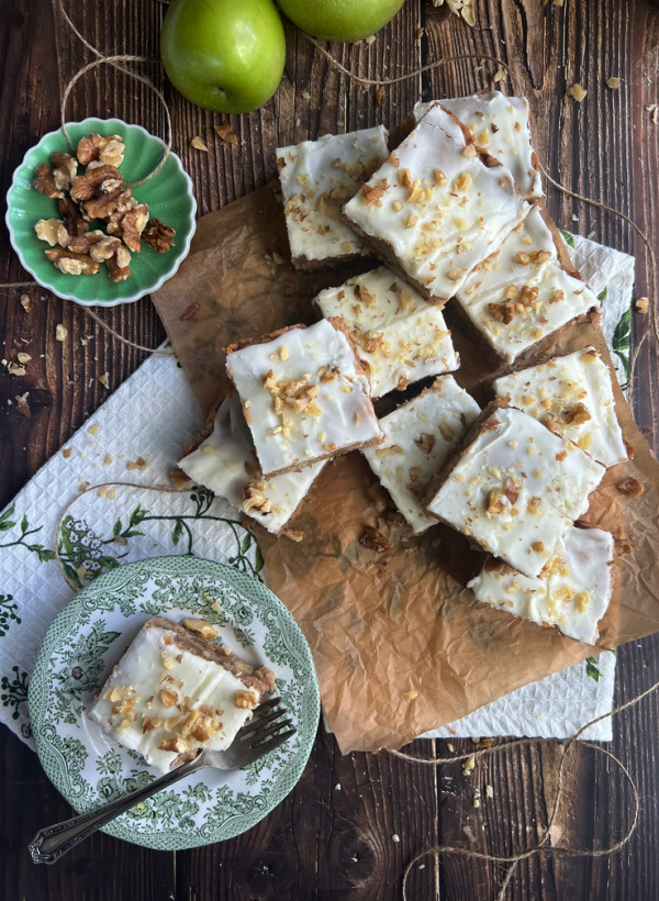 apple blondies on a pile with a green and white transfer ware plate golding a fork and a blondie.