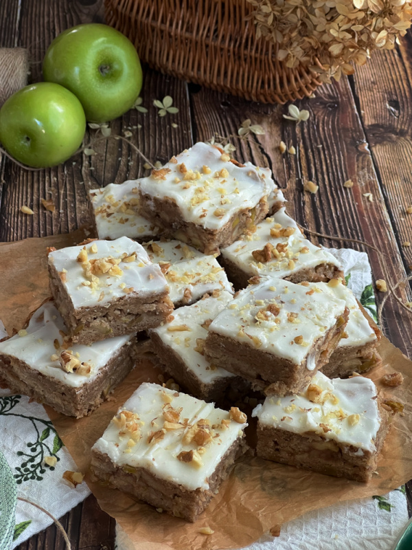cinnamon apple blondies with vanilla glaze on a pile with 2 Granny Smith apples. 