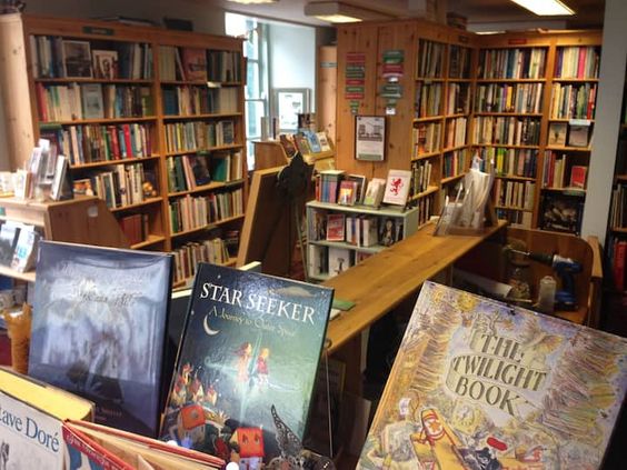 Inside of a book shop with bookcases and stacks of books. 