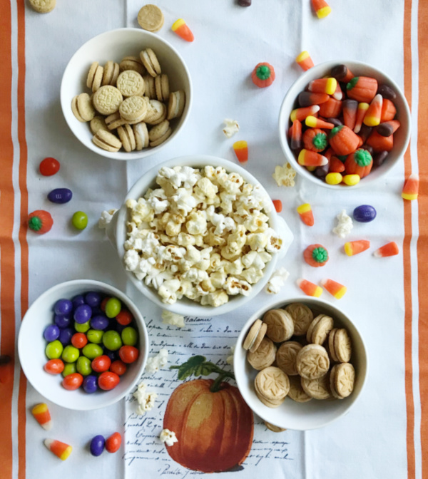 5 white bowls filled with popcorn, cookies, candy corn and m&m