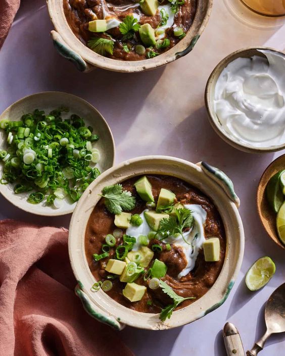 Creamy black bean soup in bowls with small bowls of cilantro, sour cream and other toppings around it. 