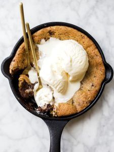 Chocolate chip cookie in a black iron skillet with a spoon and vanilla ice cream. 