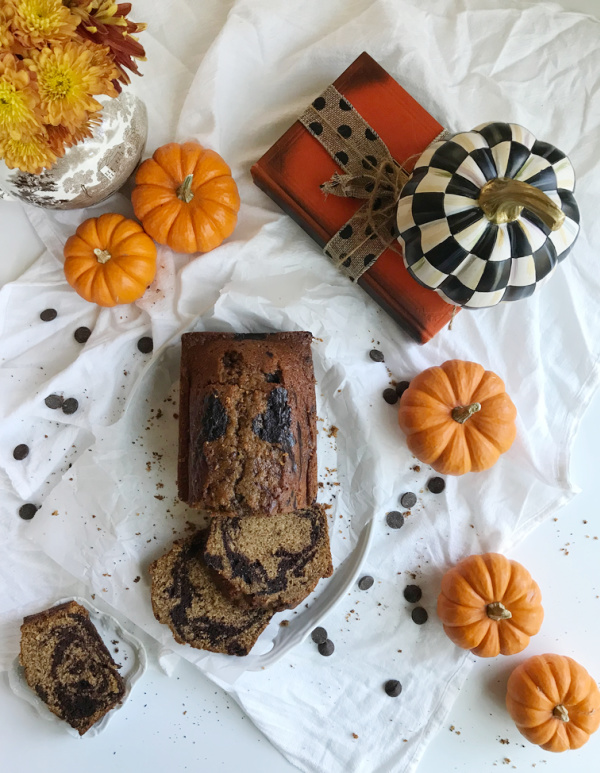 pumpkin chocolate marble bread sliced with orange pumpkins, an orange book and a black and white pumpkin scattered about. 