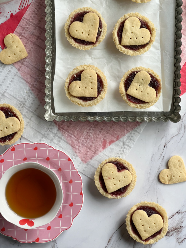 Cup of tea and raspberry frangipane tarts in a pan.