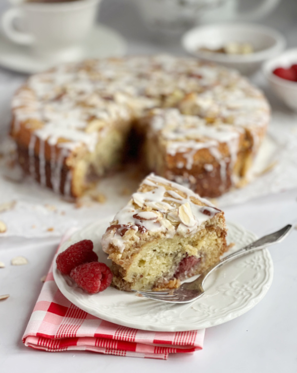 Raspberry Almond coffee cake sliced on a plate with a fork and a few fresh raspberries. 